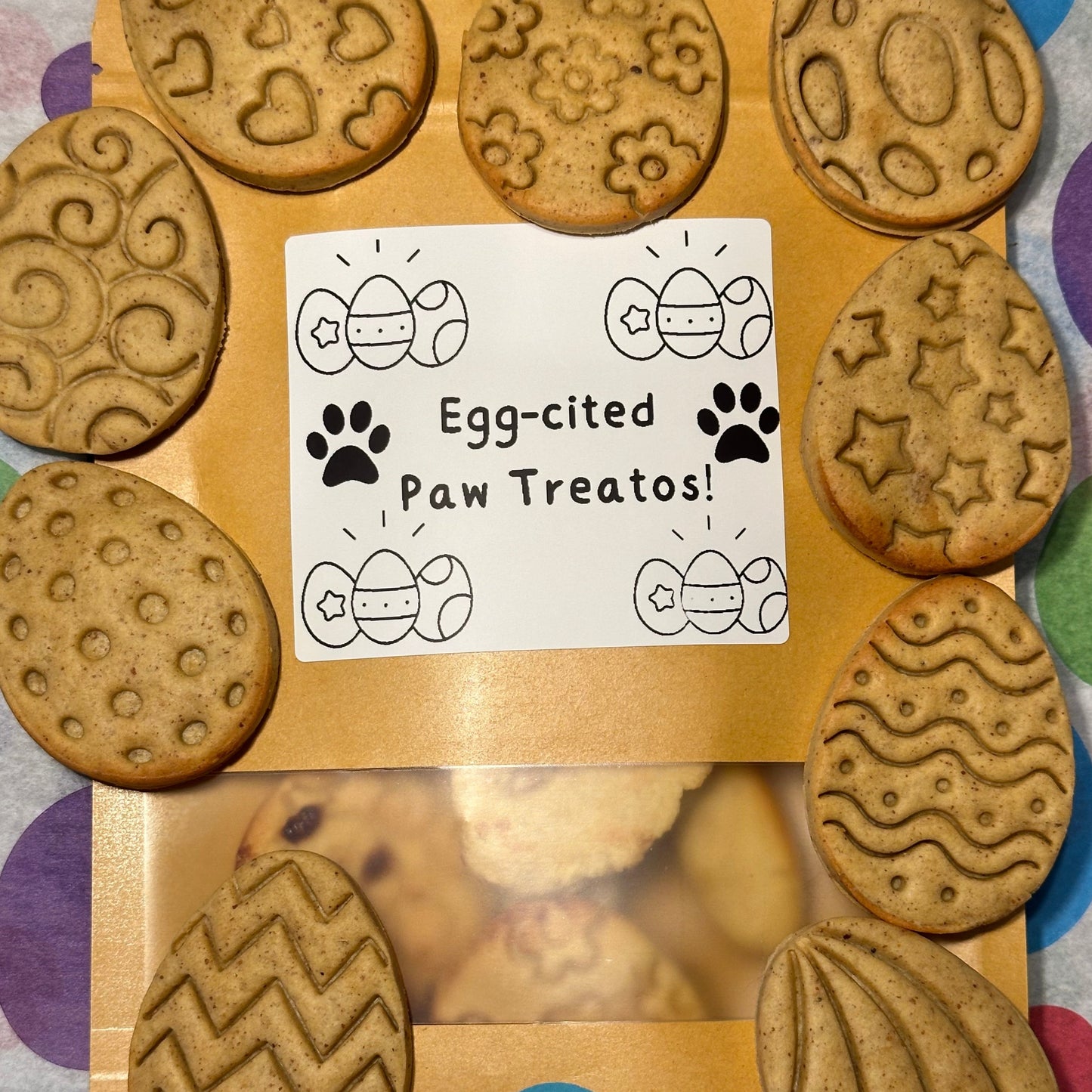 A selection of stamped Easter egg-shaped grain free dog biscuits with various patterns such as zigzag, heart, and floral designs.