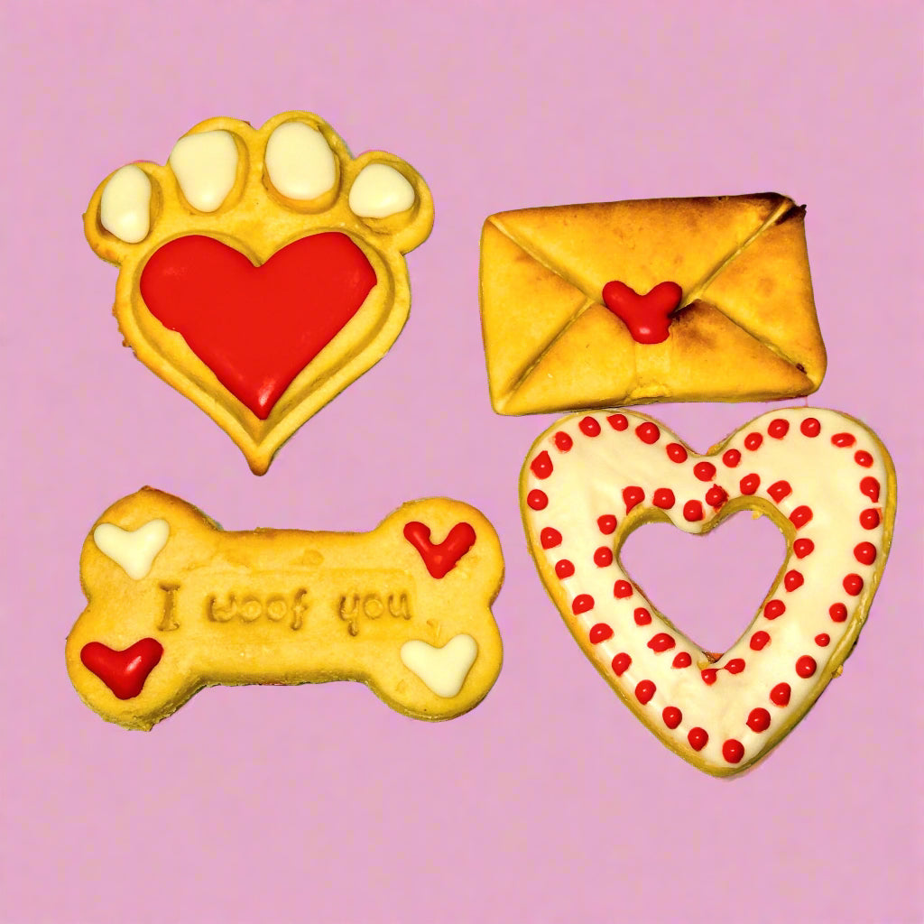 A set of dog treats shaped like a paw print, a bone, an envelope, and a heart, decorated with red and white icing