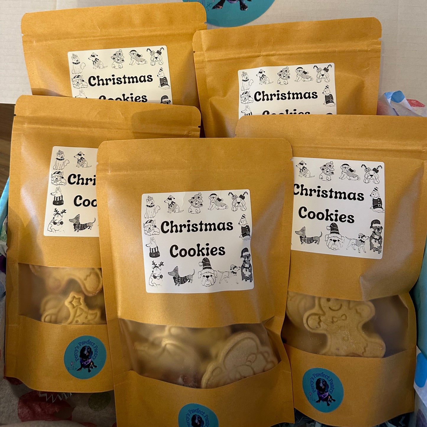 A collection of packaged Christmas-themed dog cookies with festive designs, displayed in a box.