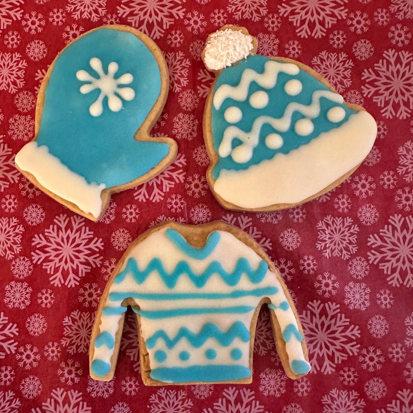 A selection of dog biscuits that are decorated in blue and white icing as bobble hats, Xmas jumpers, and mittens