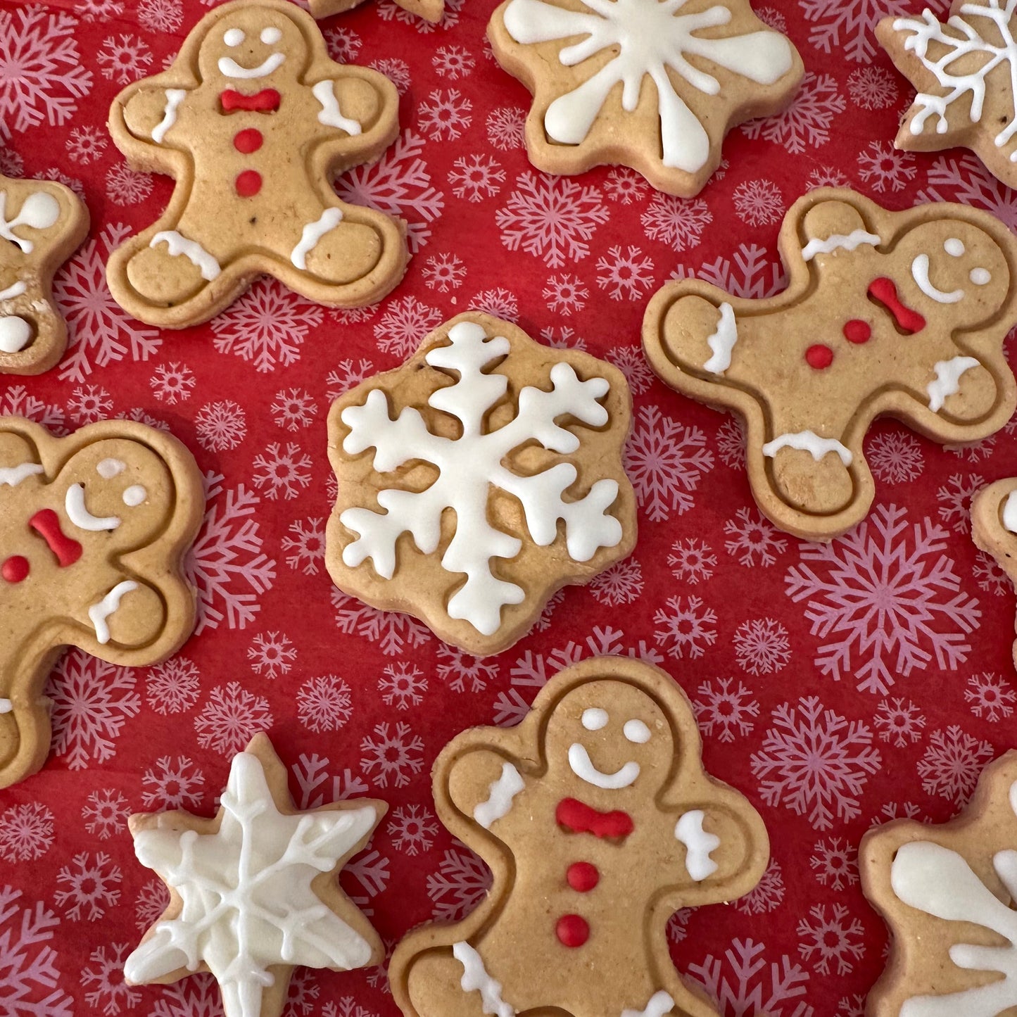 A variety of iced gingerbread man and snowflake-shaped dog treats on a red patterned surface.