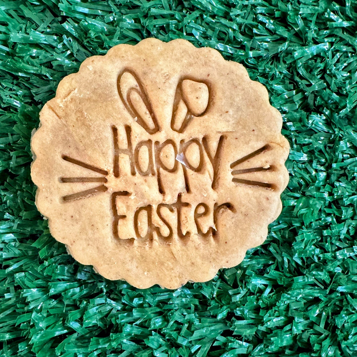 A Happy Easter dog biscuit on a green background
