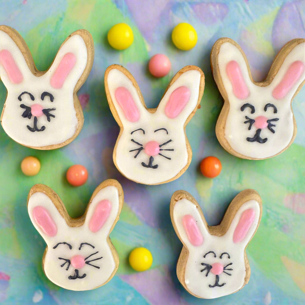 5 bunny-shaped dog biscuits decorated with dog-friendly icing, presented on a background with colourful Easter eggs.