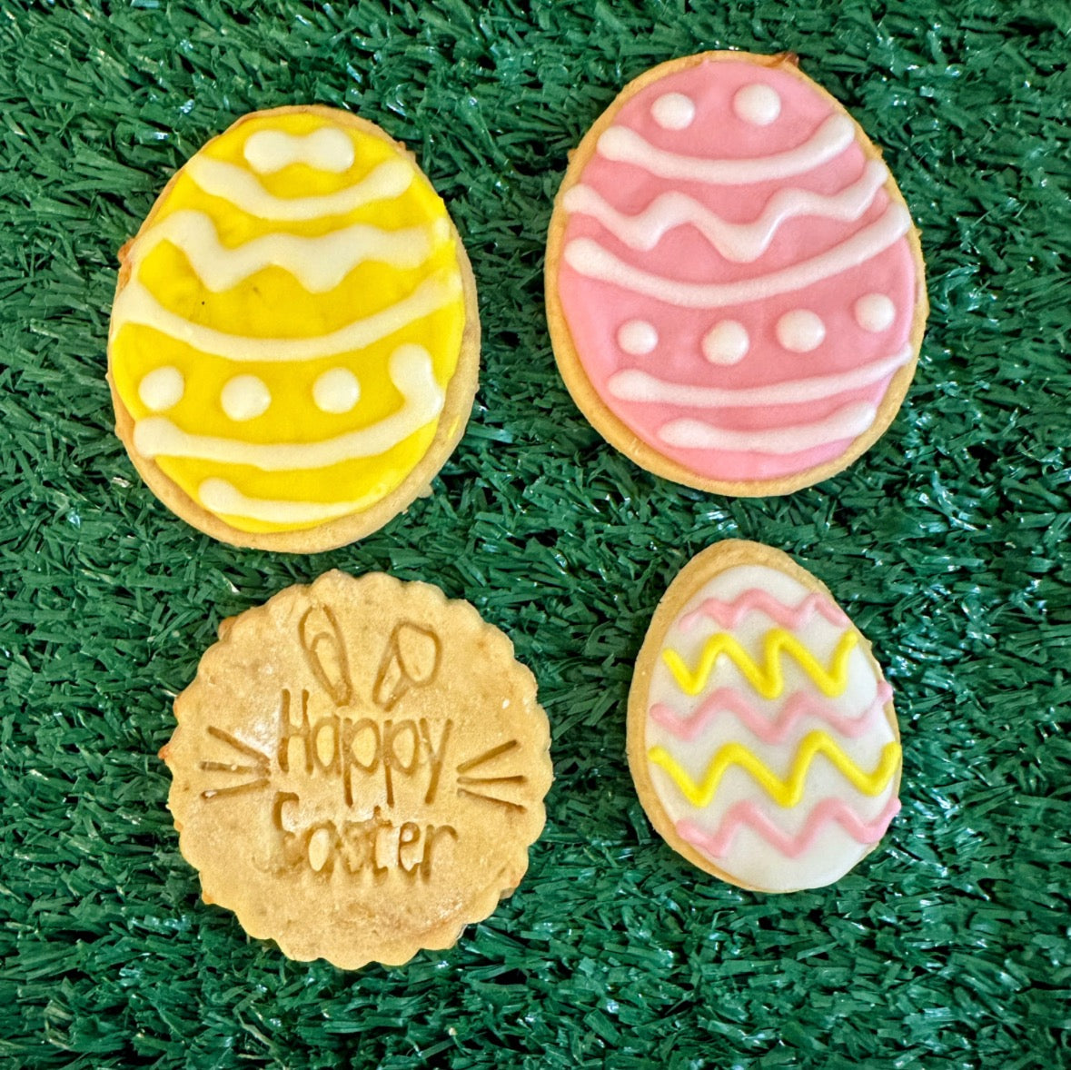 A selection of Easter-themed dog biscuits decorated to look like colorful Easter eggs, presented on a green backgorund