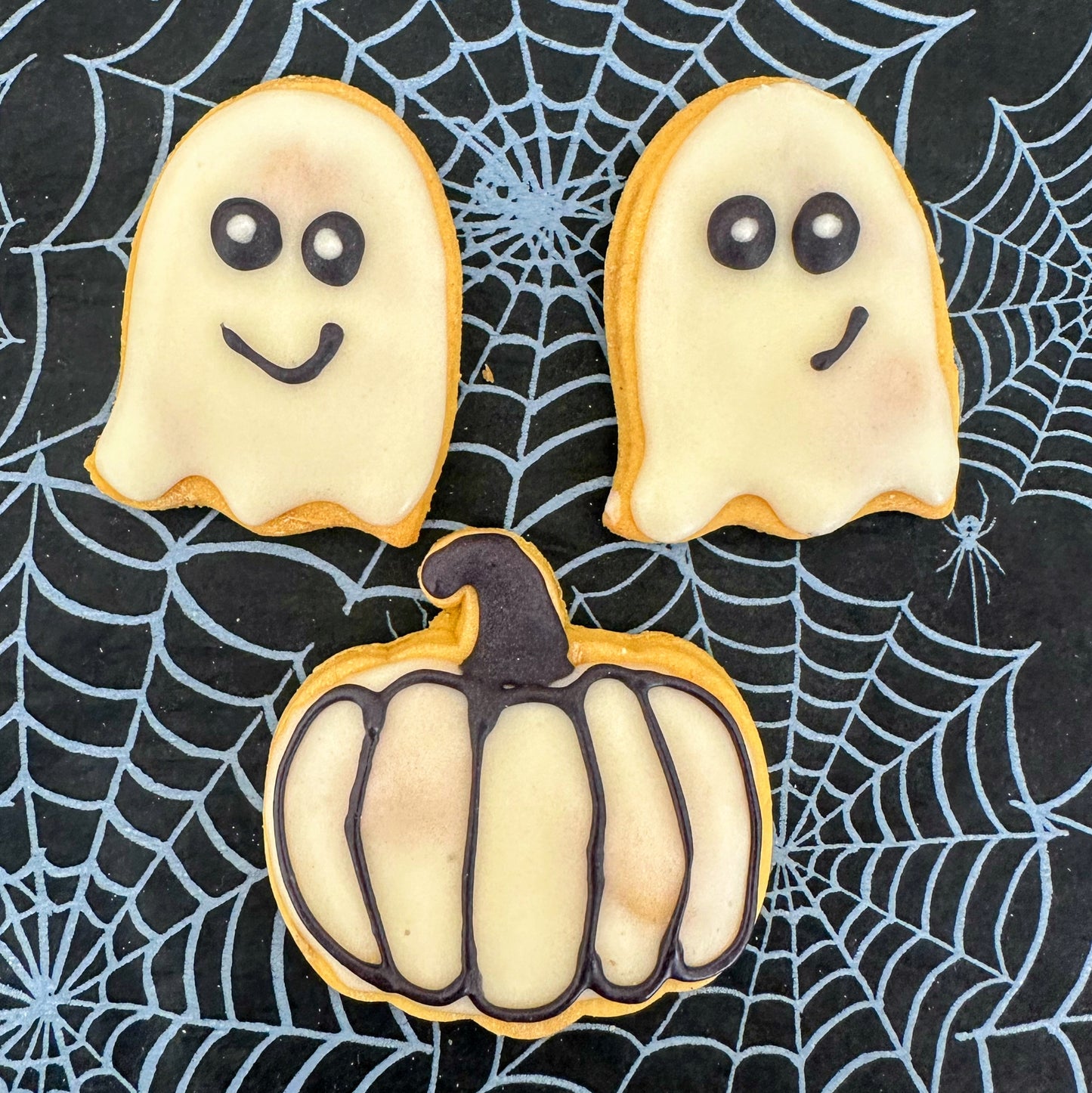 Halloween-themed cookies shaped like ghosts and a pumpkin on a spider web background