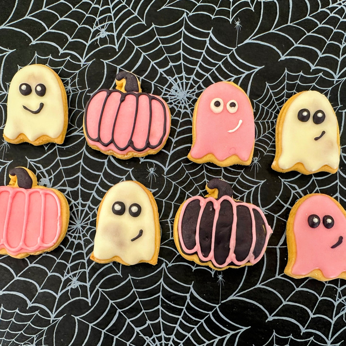Halloween-themed cookies shaped like ghosts and pumpkins on a spider web background