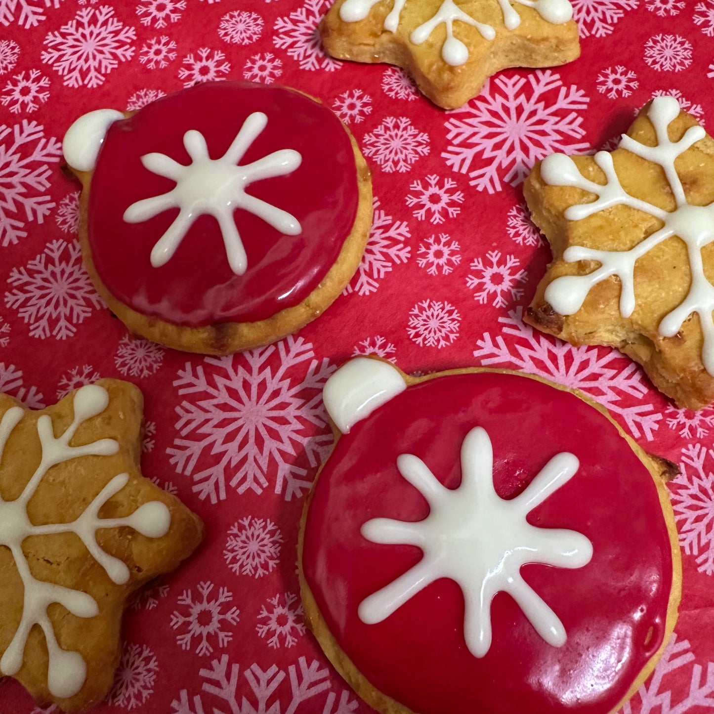 Decorative cookies with red and white icing on a pink snowflake patterned background