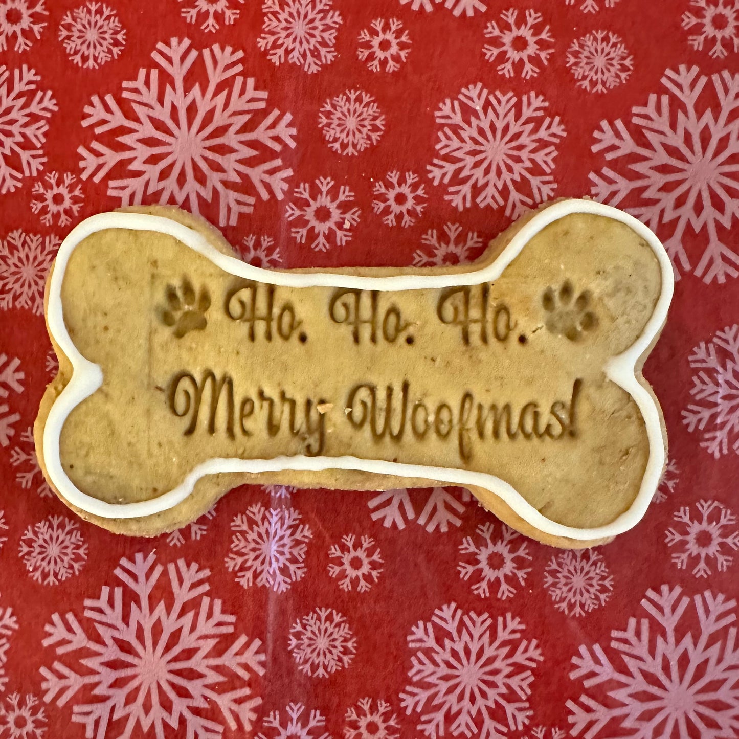 A dog bone-shaped biscuit with the text 'Ho, Ho, Ho Merry Woofmas!' on a red and white patterned background.
