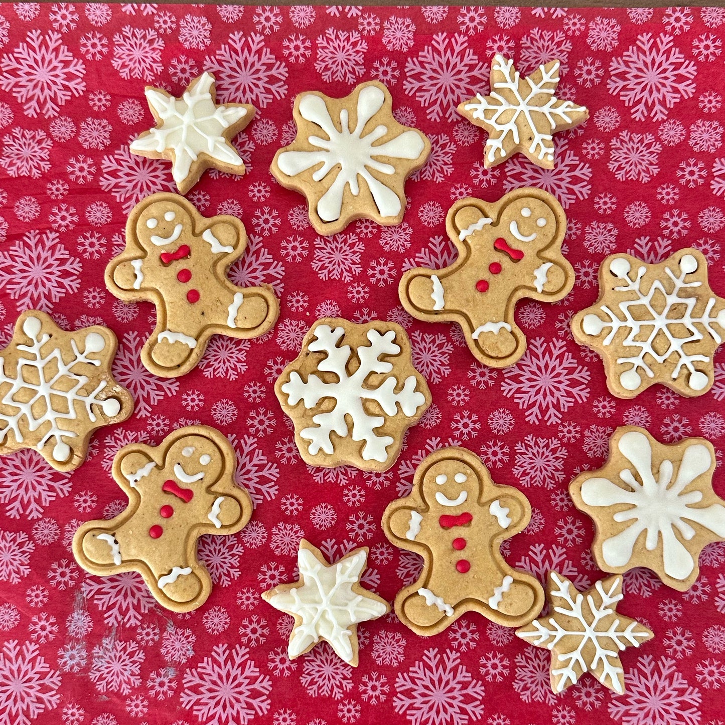 A variety of iced gingerbread man and snowflake-shaped dog treats on a red patterned surface.