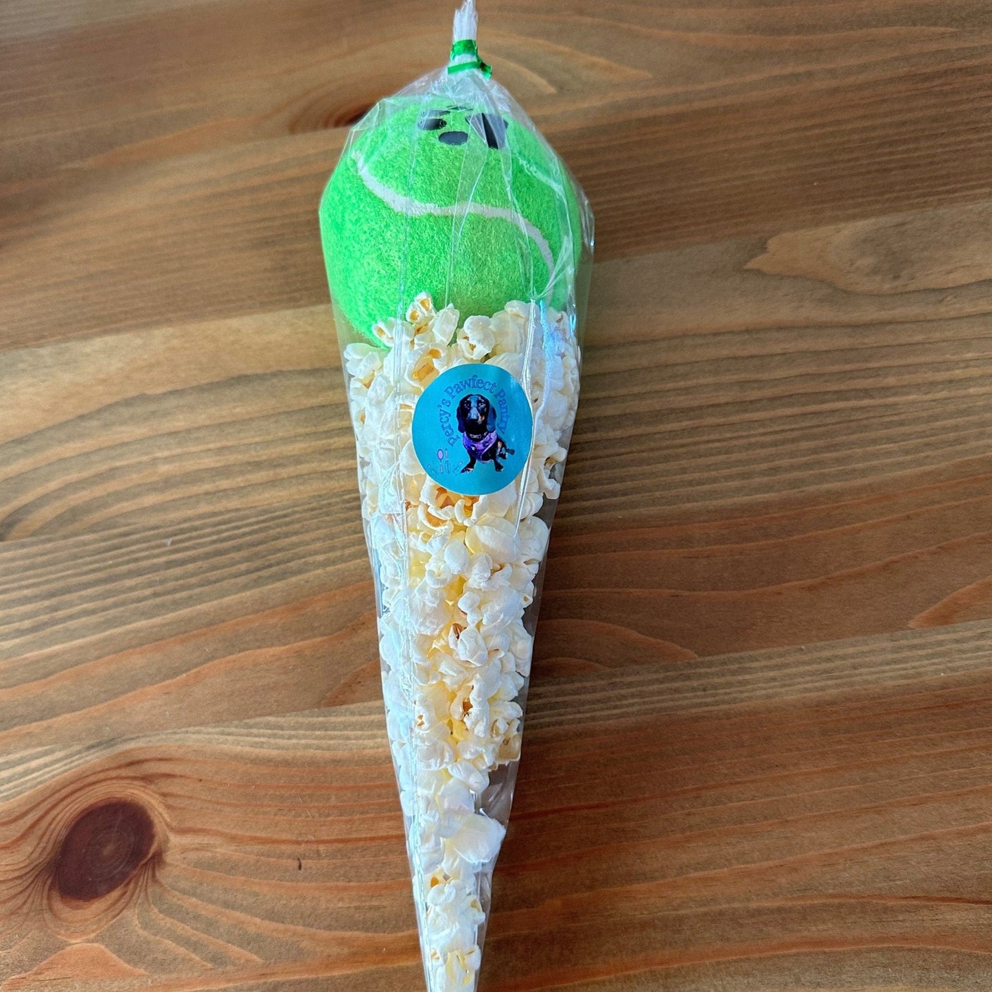 A treat cone of pupcorn topped with a tennis ball