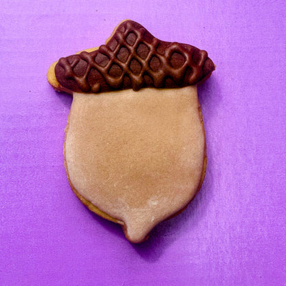 Acorn-shaped cookie with brown acrylic on a purple background