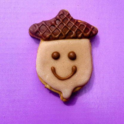 Cookie shaped like an acorn with a smiley face on a purple background
