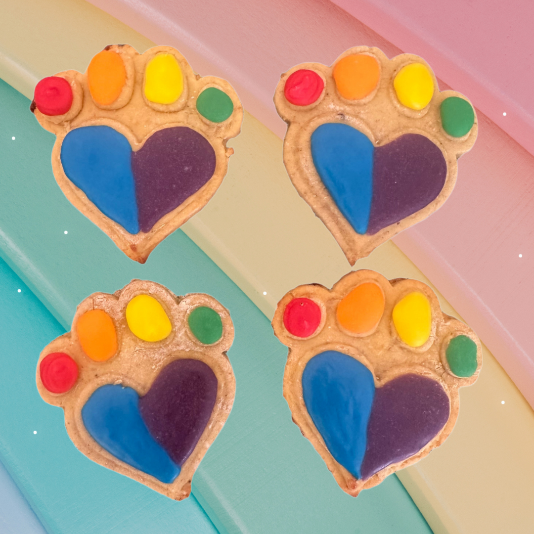 Four rainbow-colored paw print cookies on a colorful background