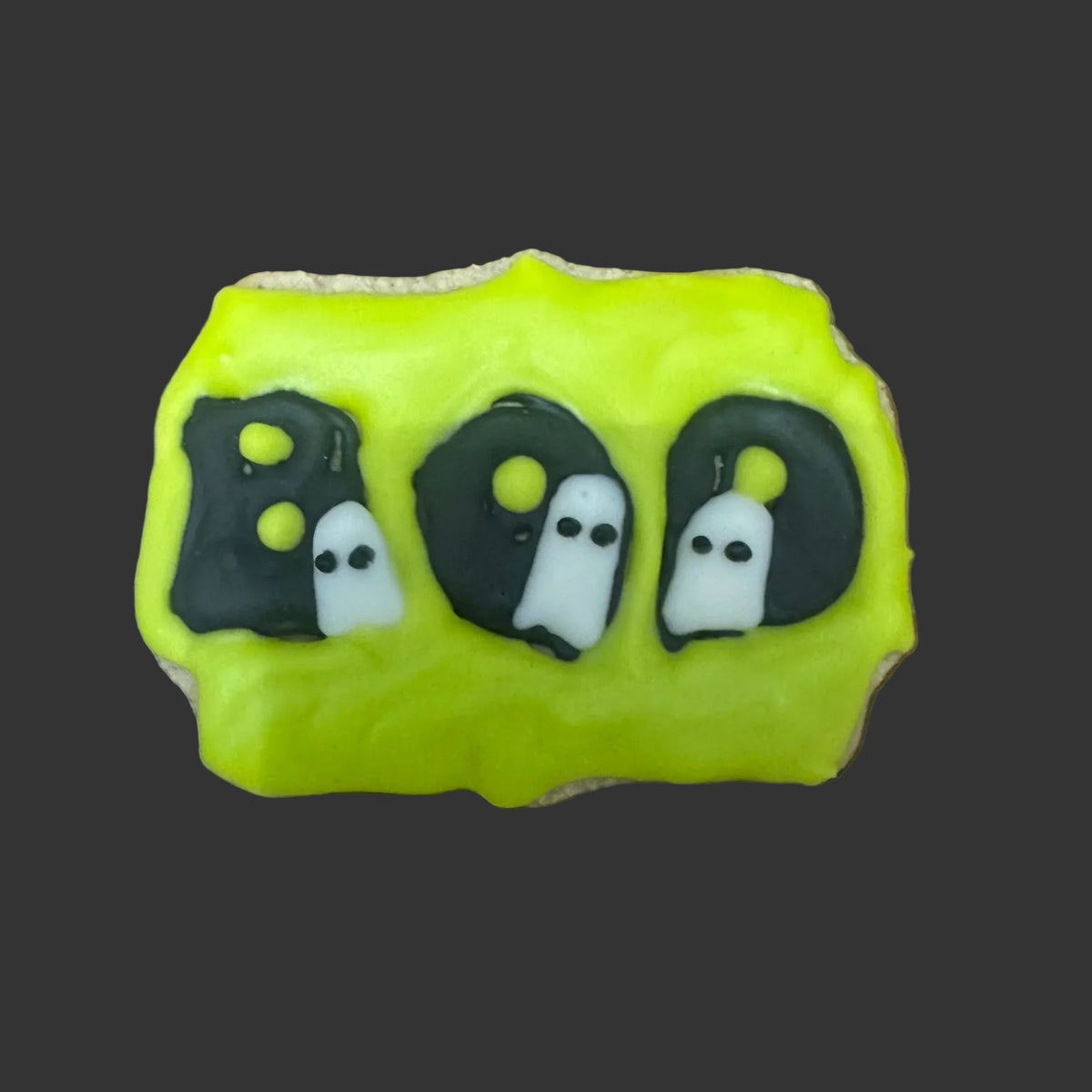 A Halloween-themed cookie decorated with bright green icing and the word 'BOO' in black with 3 ghosts