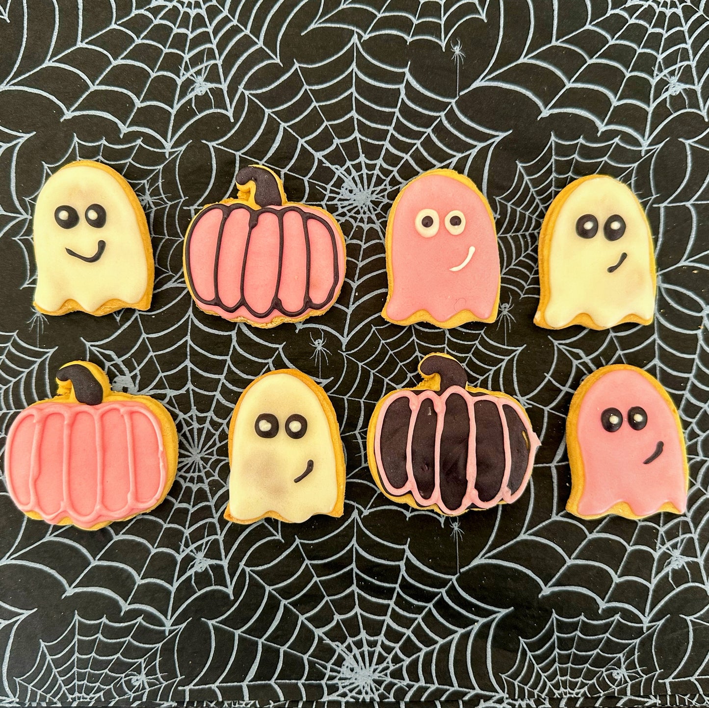 Halloween-themed cookies shaped like ghosts and pumpkins on a spider web background