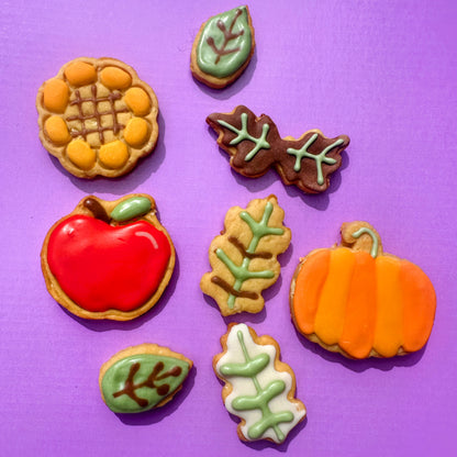 Decorative cookies shaped like a pumpkin, apple, and leaves on a purple background