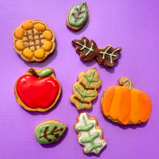 Decorative cookies shaped like a pumpkin, apple, and leaves on a purple background