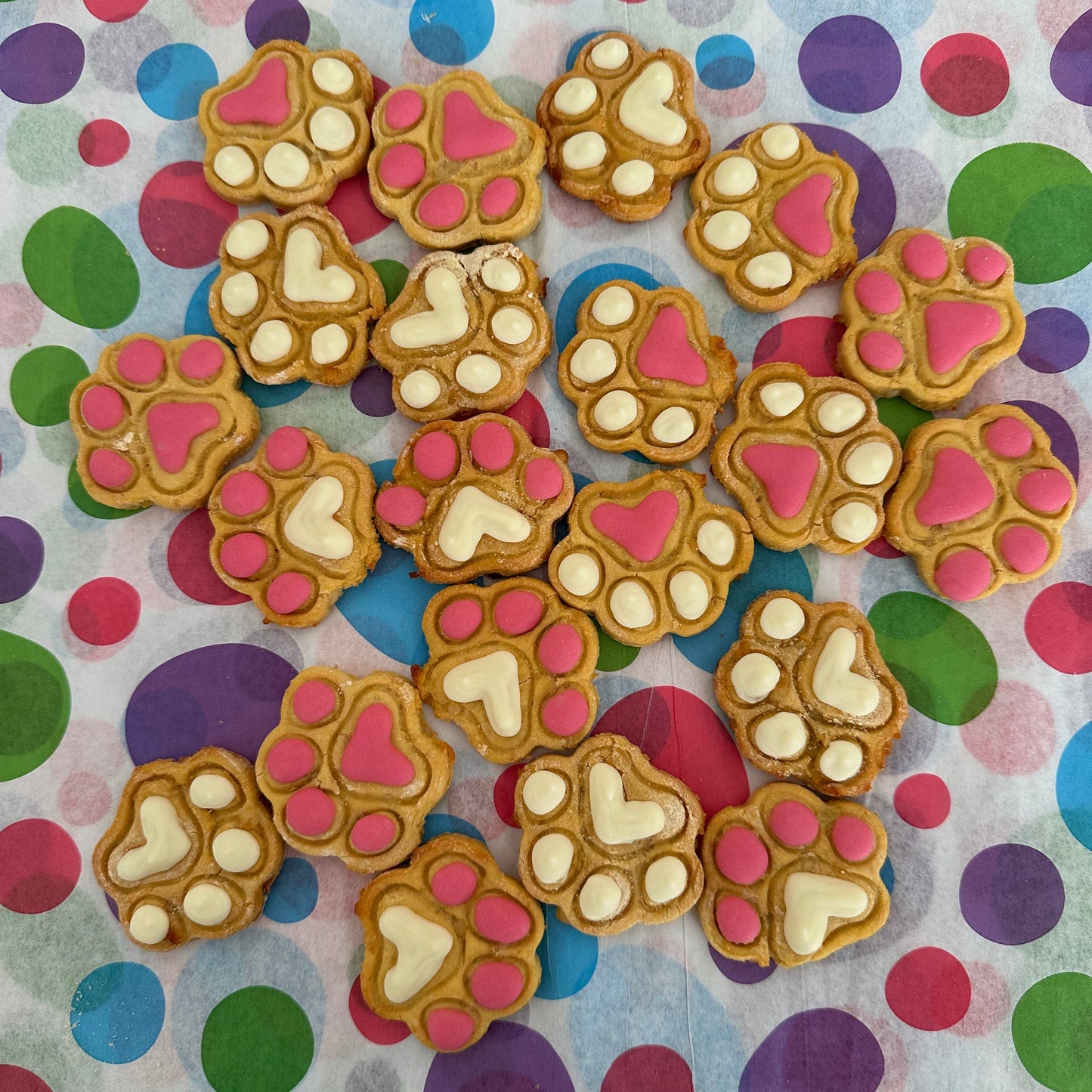 A selection of mini paw print dog biscuits decorated with pink and white icing