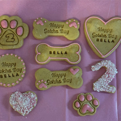 Collection of personalized dog treats with names and 'Happy Gotcha Day' text on a pink background