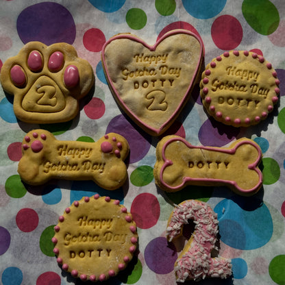 Dog treats shaped like a paw, heart, bone, and donut with 'Happy Getcha Day Dotty' text on a polka dot background.