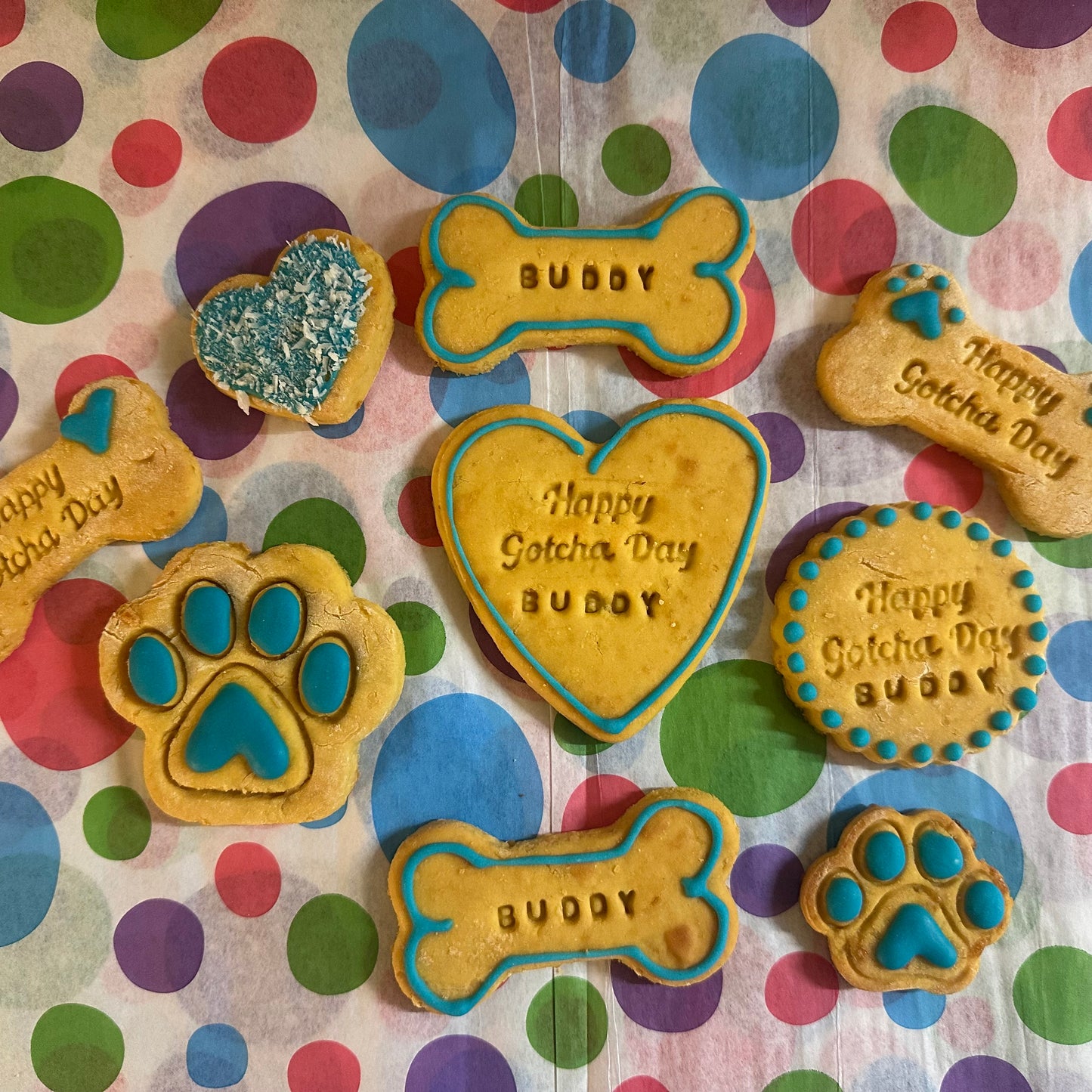 Dog treats shaped like bones, hearts, and paws with 'Happy Gotcha Day Buddy' text on a polka dot background.