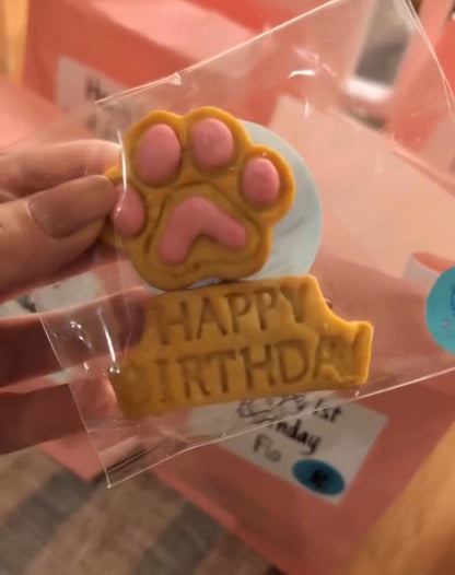 Dog birthday cookie with paw print and 'Happy Birthday' text in clear packaging.