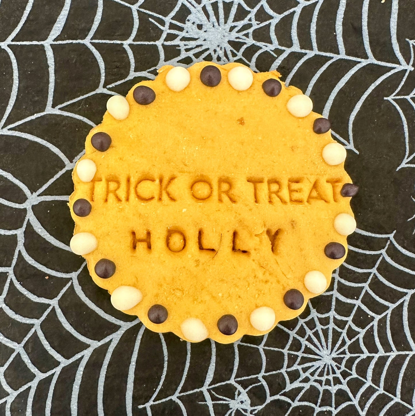 Cookie with 'TRICK OR TREAT HOLLY' text on a spider web background