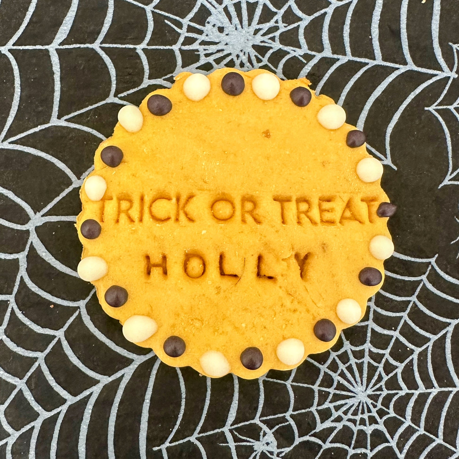 Cookie with 'TRICK OR TREAT HOLLY' text on a spider web background