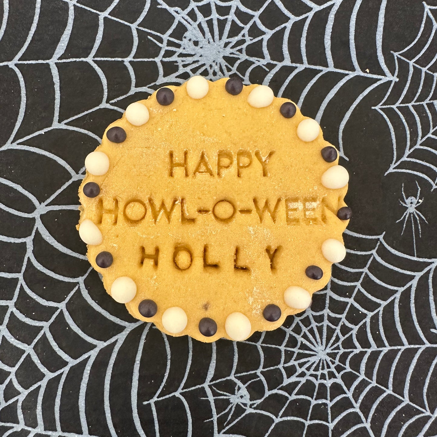 Cookie with 'Happy Howl-o-Ween Holly' text on a spider web background