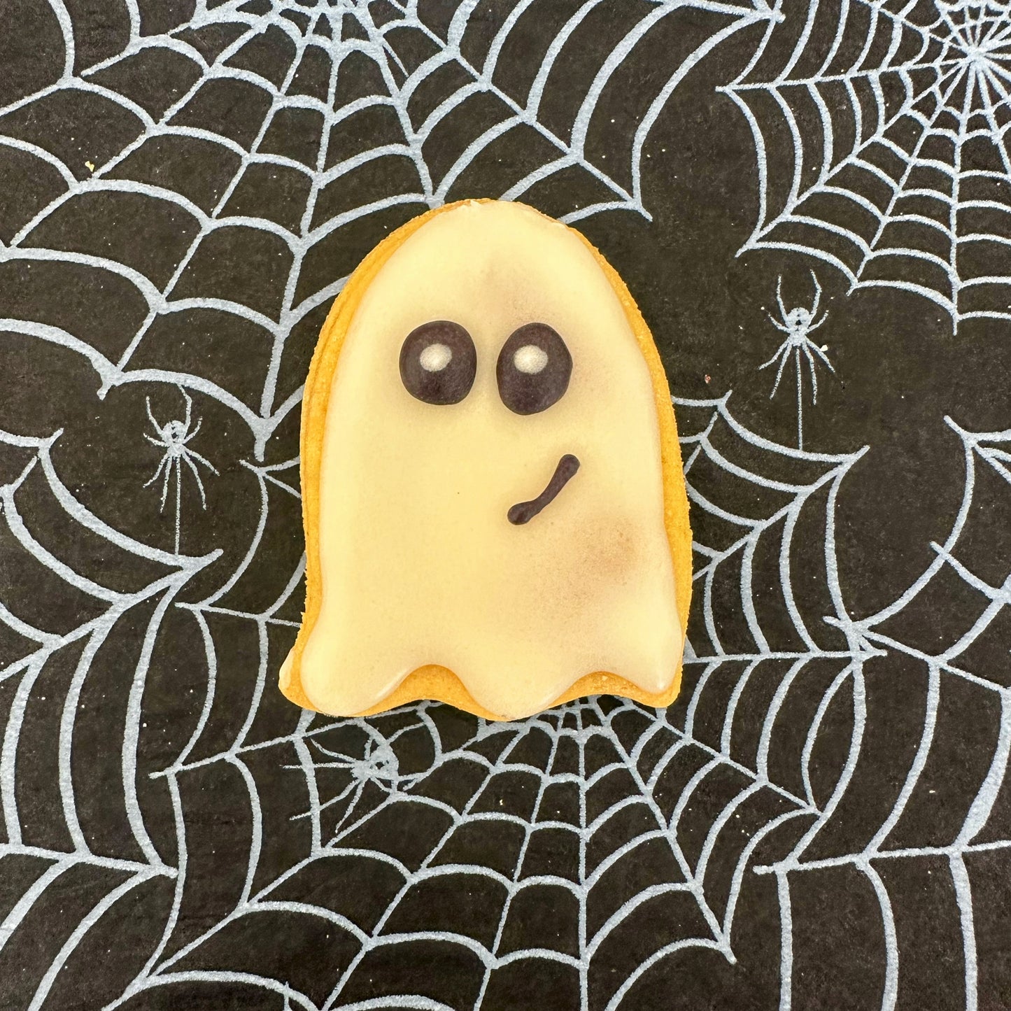 Halloween-themed cookie shaped like a ghost on a spider web background
