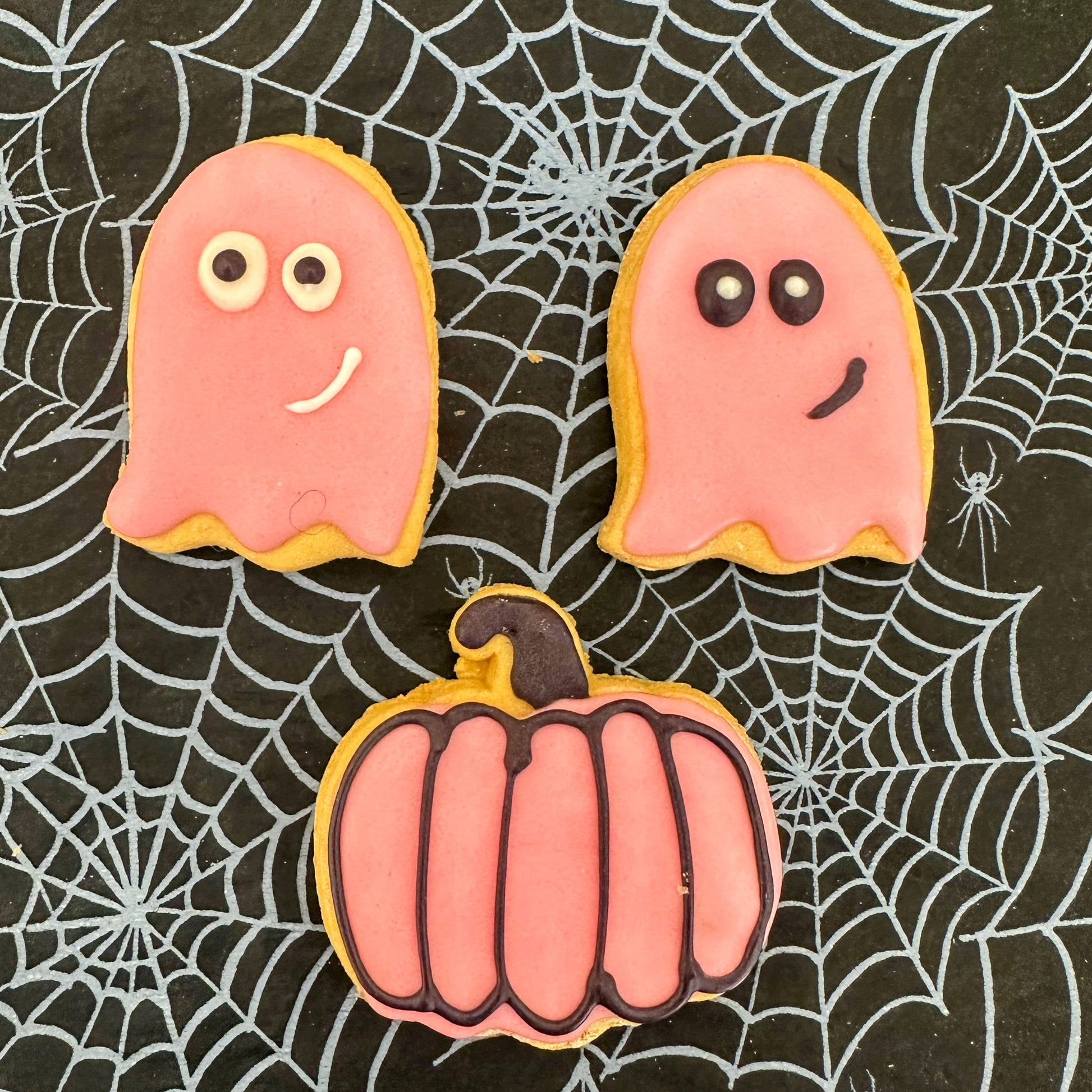 Halloween-themed cookies shaped like ghosts and a pumpkin on a spider web background