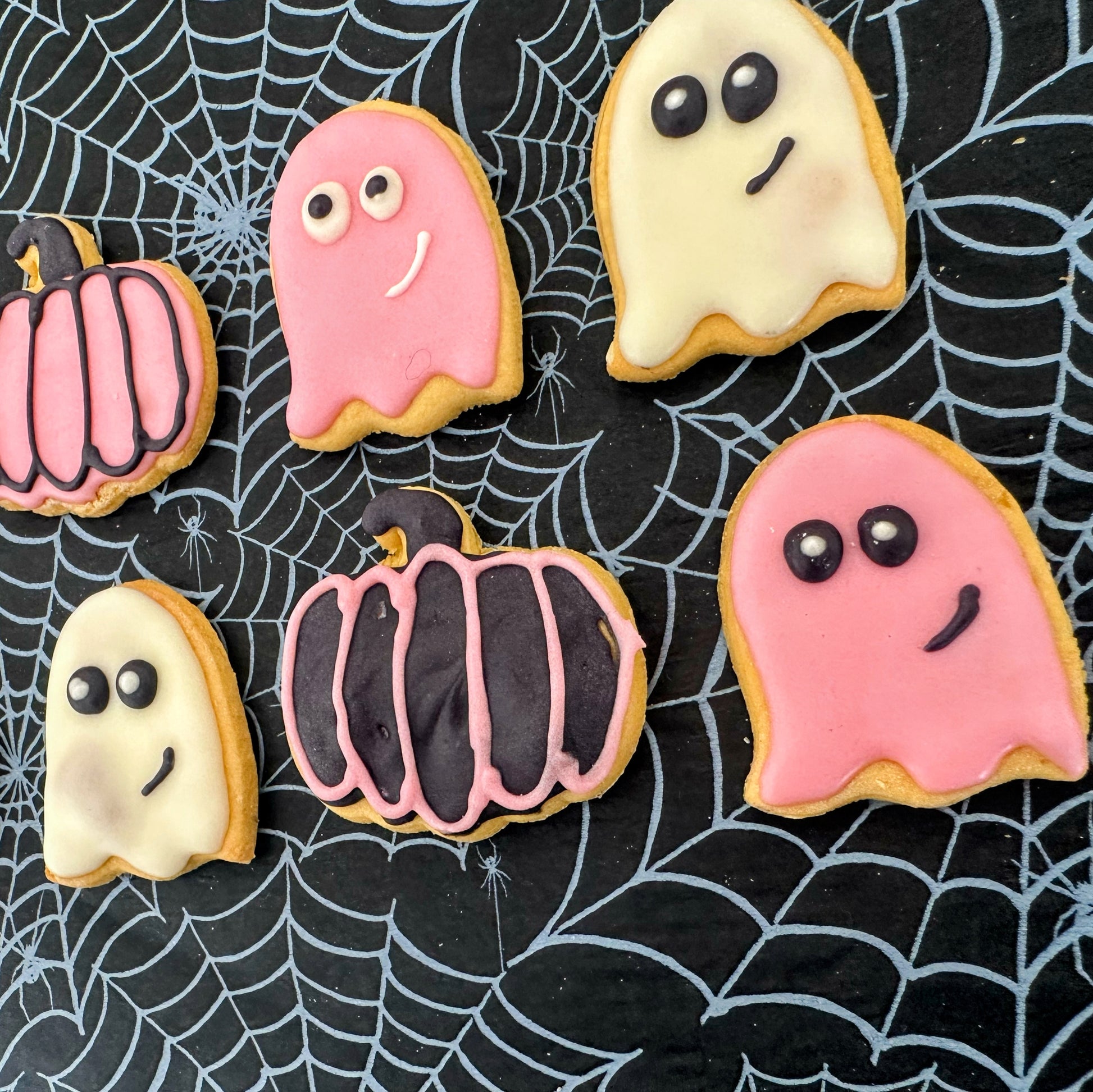 Halloween-themed cookies shaped like ghosts and pumpkins on a spider web background