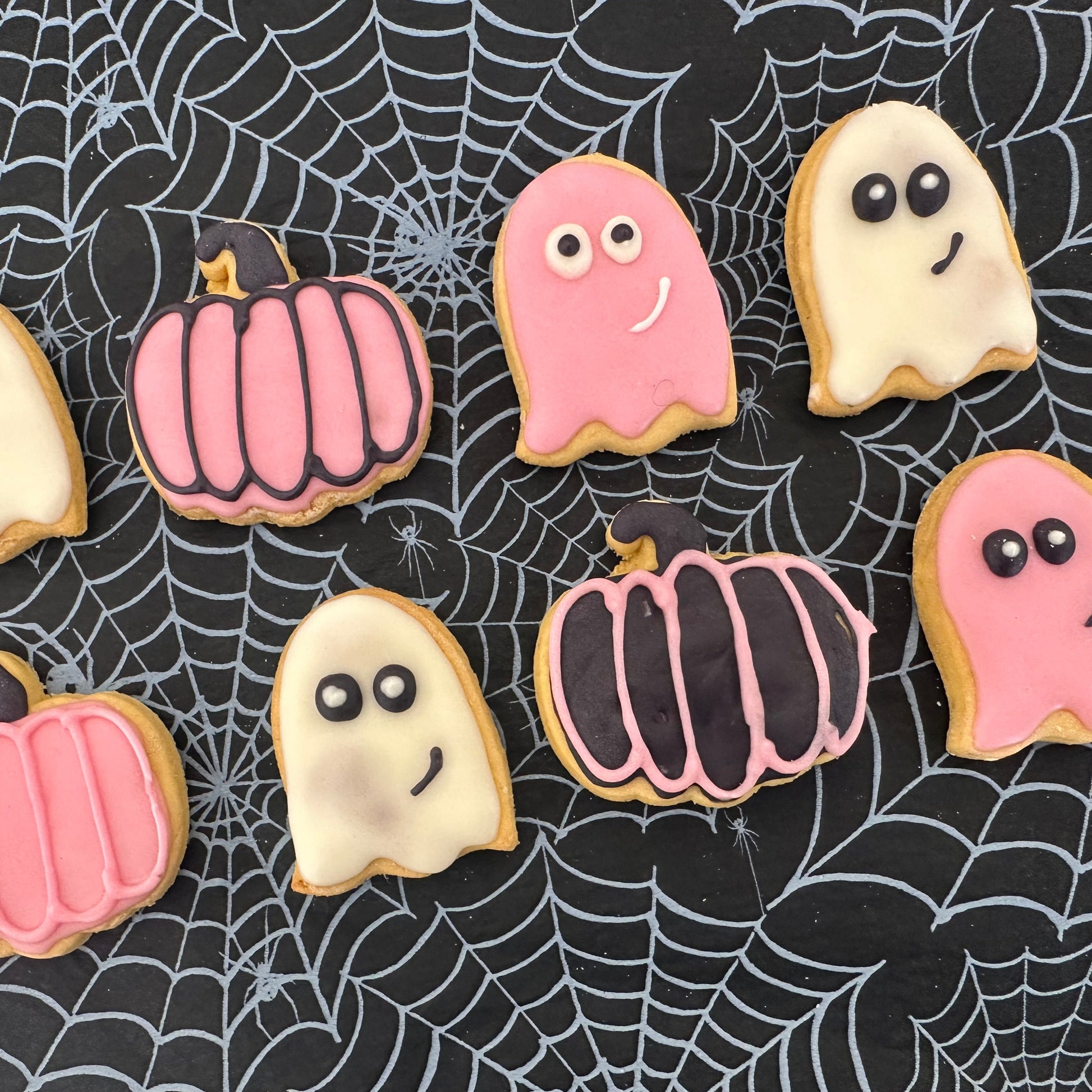 Halloween-themed cookies including ghosts and pumpkins on a spider web background