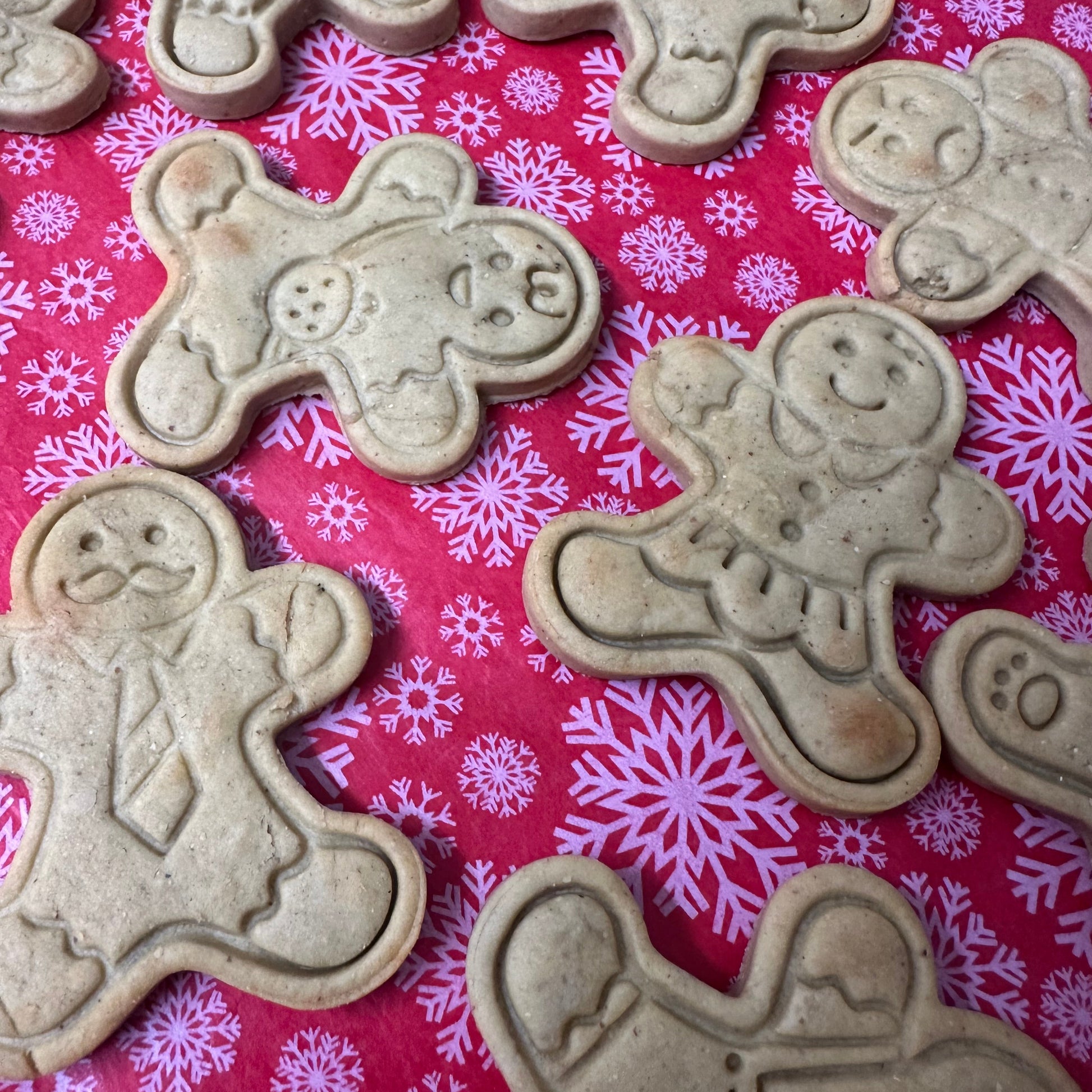 Gingerbread men cookie cutters on a pink background with snowflake patterns