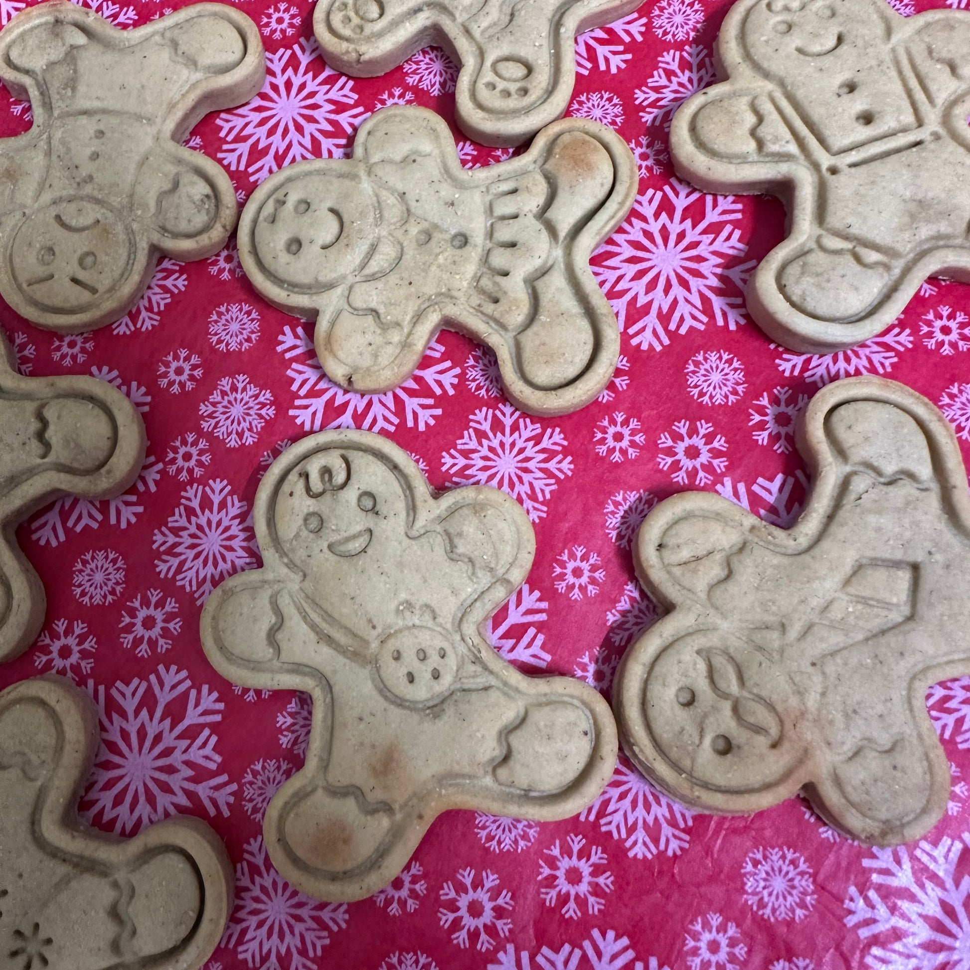 Biscuit cutters shaped like gingerbread characters on a pink background with snowflake patterns