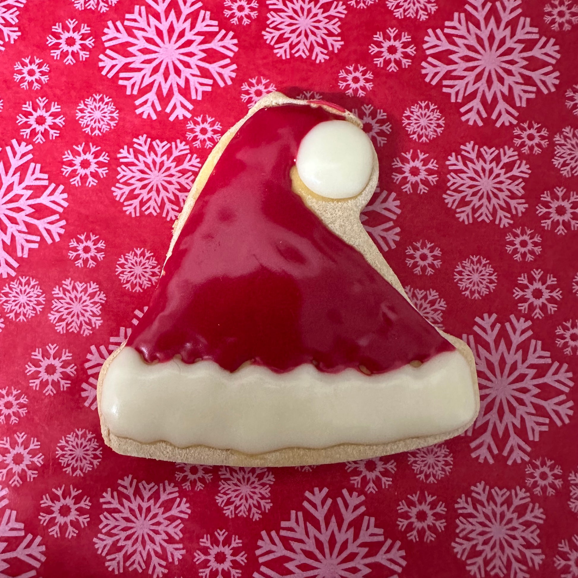 Cookie shaped like a Santa hat on a red background with white snowflakes