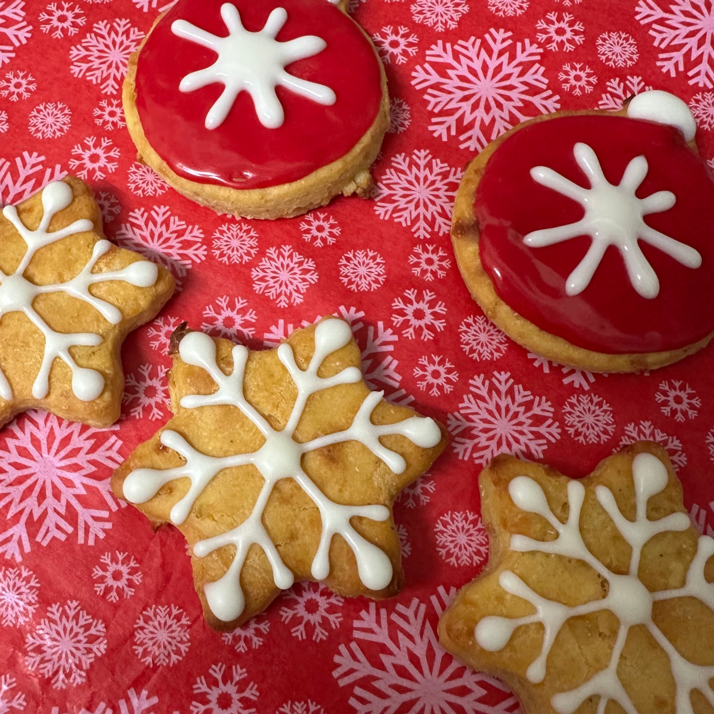 Decorative cookies with red icing and white snowflake designs on a red background with snowflake patterns.