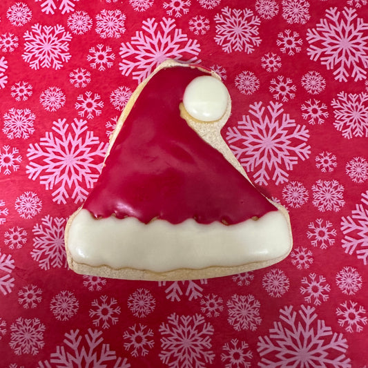 Cookie shaped like a Santa hat on a red background with white snowflakes