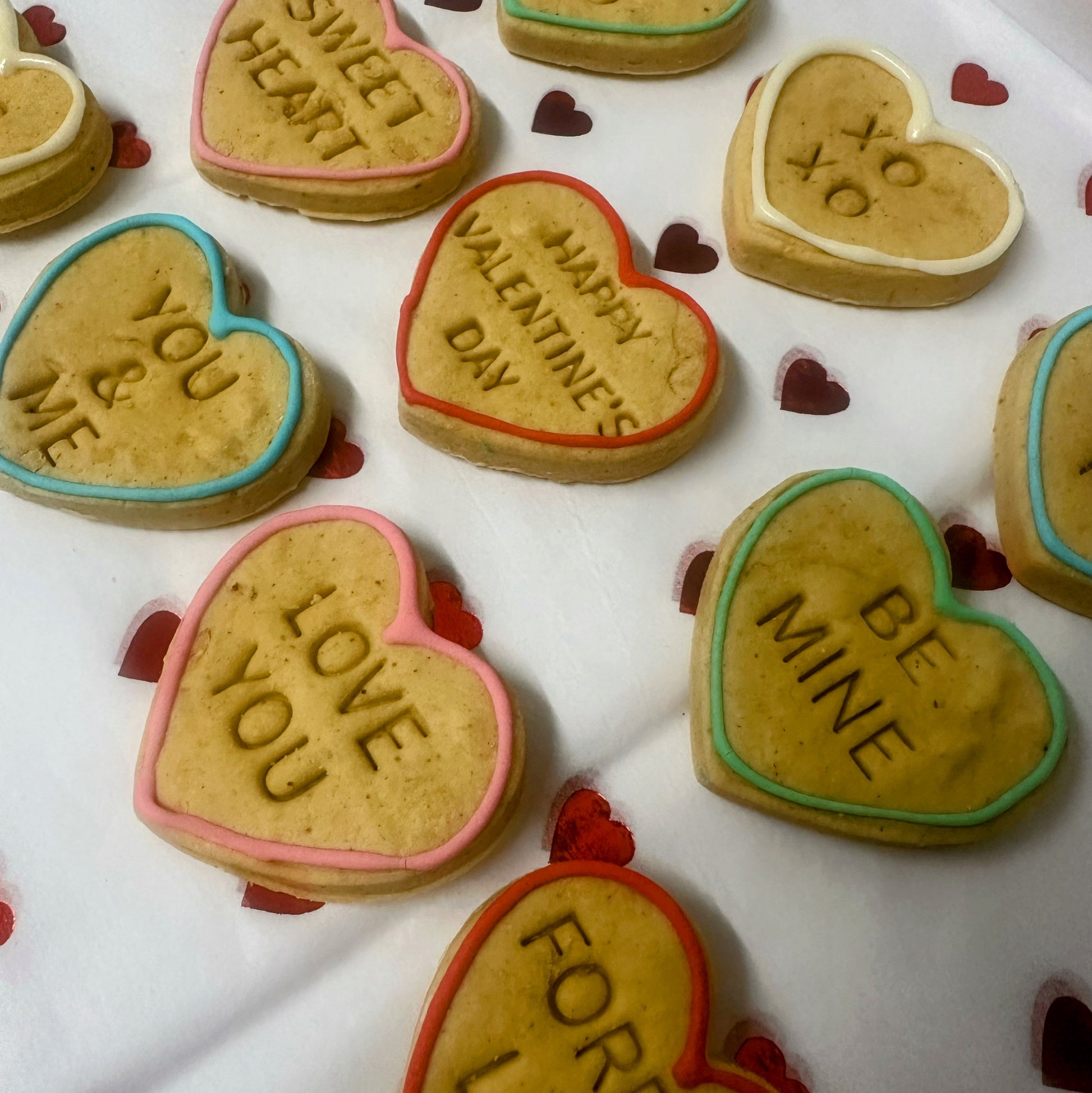 Heart-shaped cookies with Valentine's Day messages on a white surface.