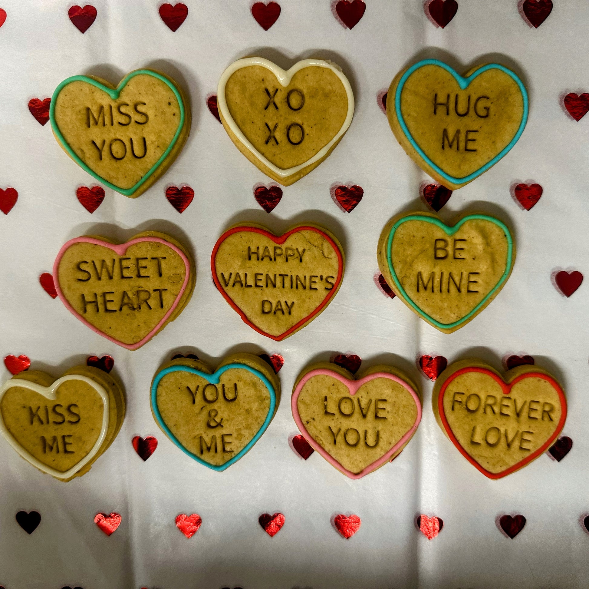 Heart-shaped cookies with Valentine's Day messages on a white background with red heart decorations.