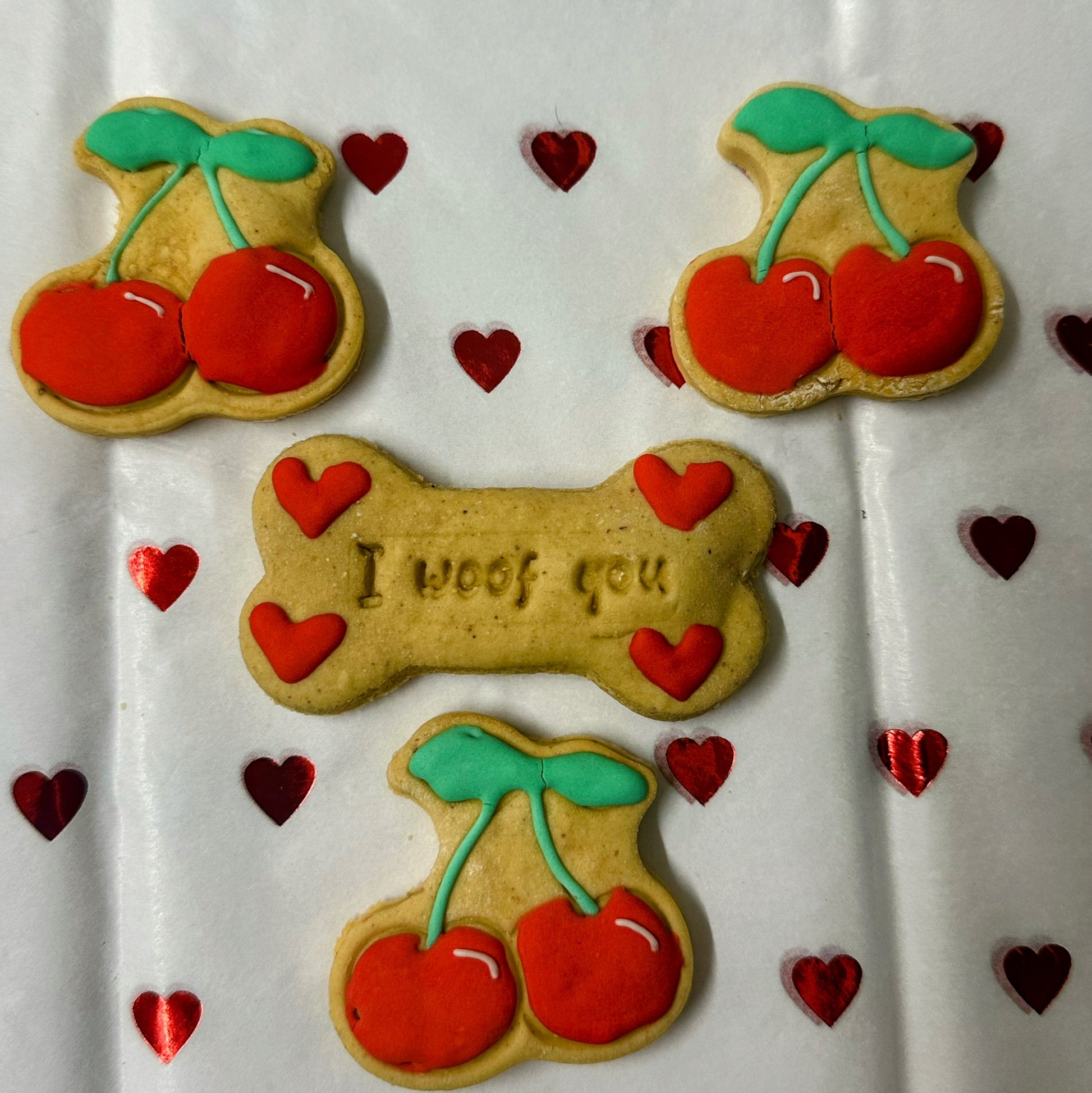 Dog treats shaped like bones and cookies with cherries on a white background with heart decorations.