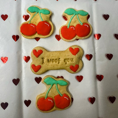 Decorative cookies with cherries and a bone-shaped cookie with 'I woof you' text on a heart-patterned background.