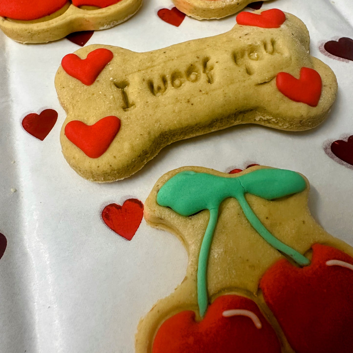 Dog bone-shaped cookies with 'I woof you' text and red hearts on a white tray.