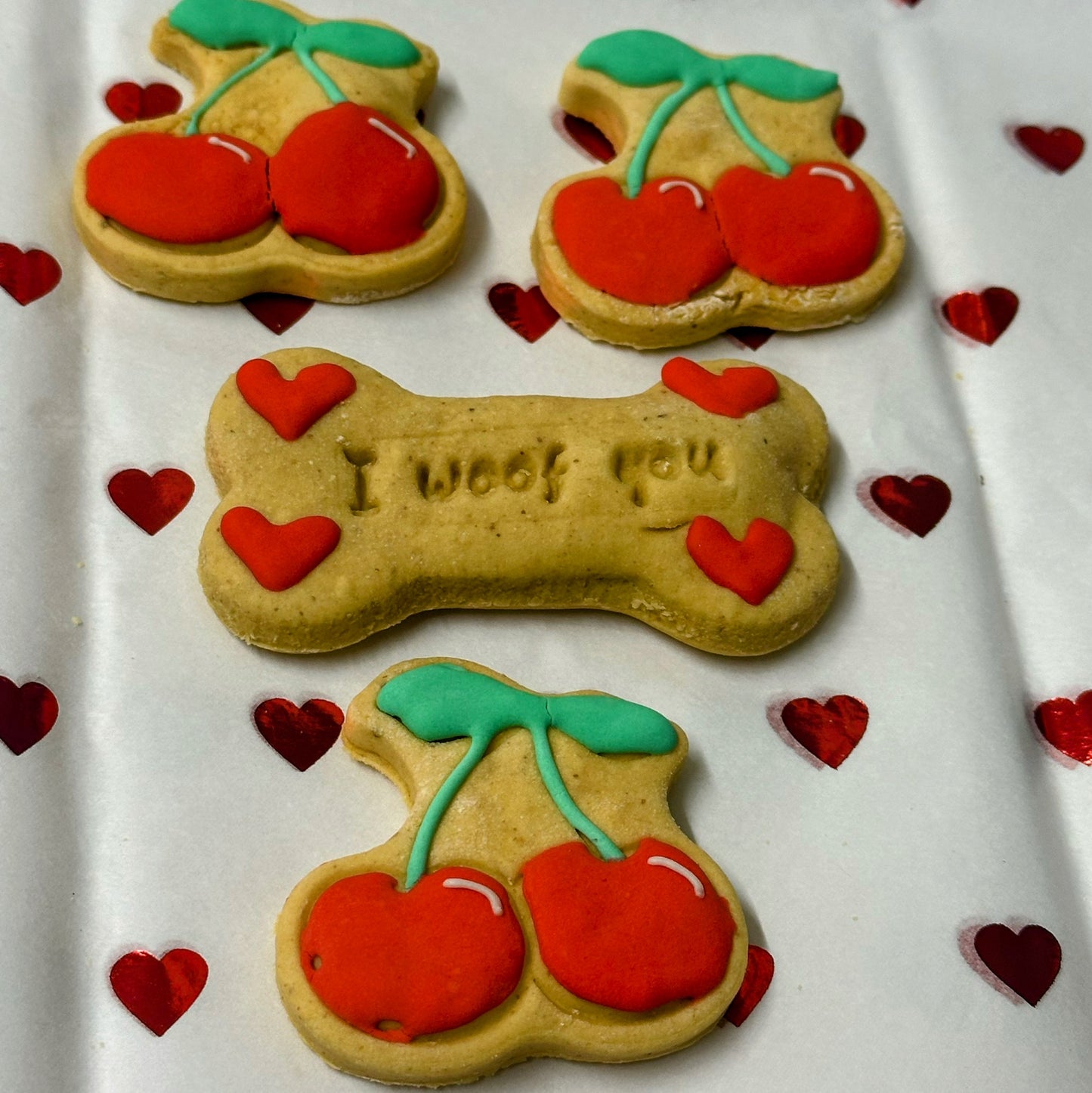 Dog treats shaped like bones and cherries with 'I woof you' text on a heart-patterned background.