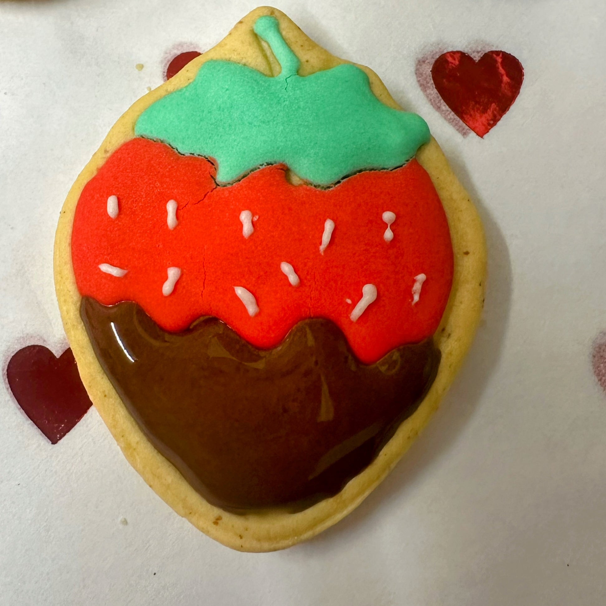 Acute strawberry-shaped biscuits with red icing, green tops, and chocolate-dipped bottoms