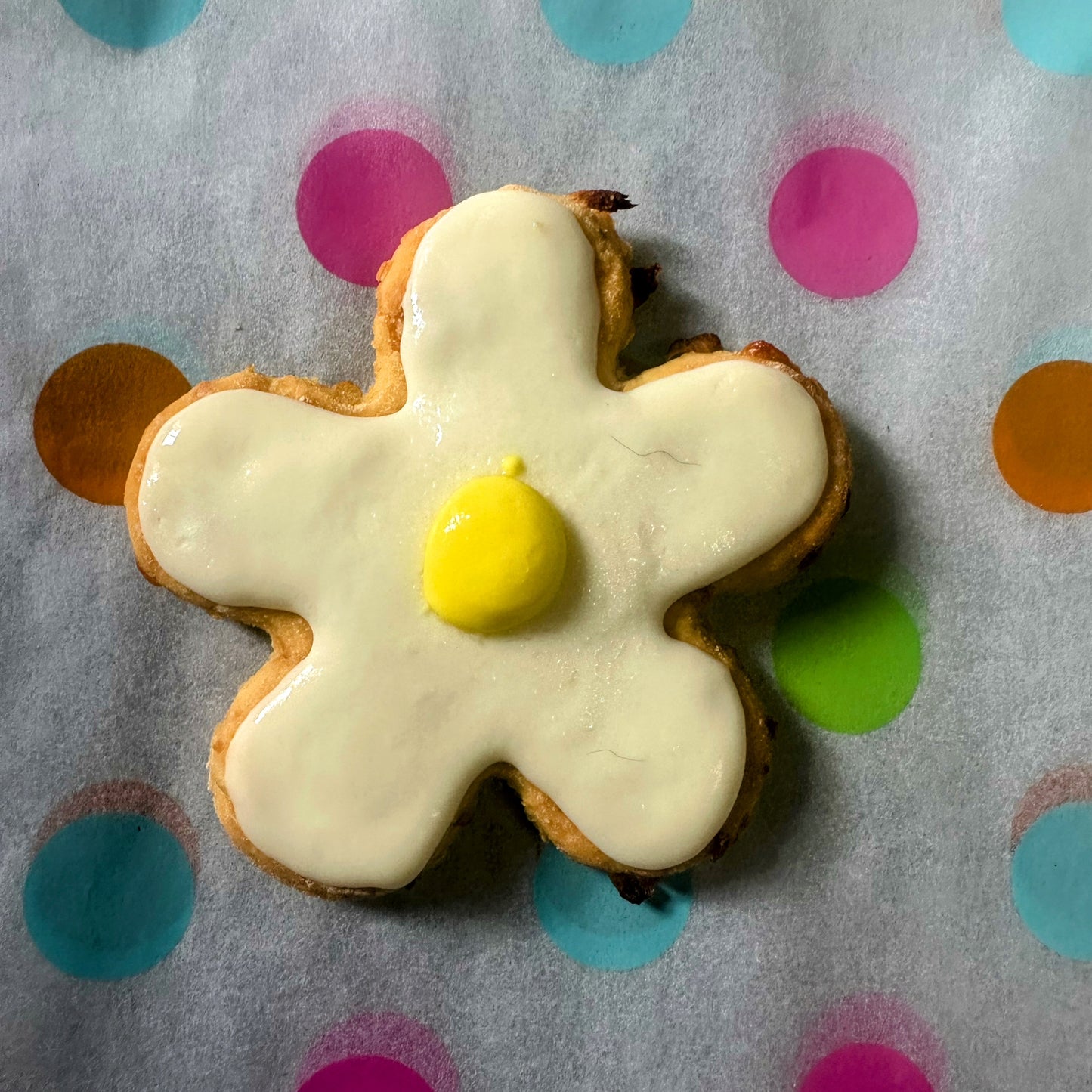 Cookie shaped like a flower with white icing and yellow center on polka dot background