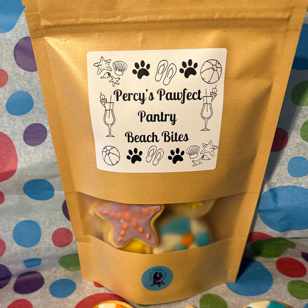 A bag of 'Percy's Pawfect Pantry' dog treats with 'Beach Bites' label, featuring illustrations of a dog, basketball, and beach items. The bag is adorned with a paw print and sand design, suggesting a beach-themed product.