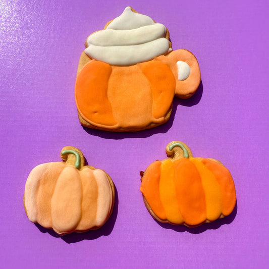 Three pumpkin-shaped cookies with white frosting on a purple background