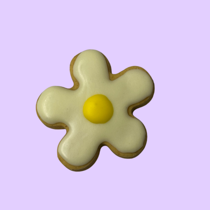 Flower-shaped cookie with white icing and a yellow center on a light purple background