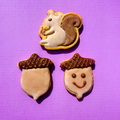 Three cookie decorations shaped like a squirrel, an acorn, and a face on a purple background